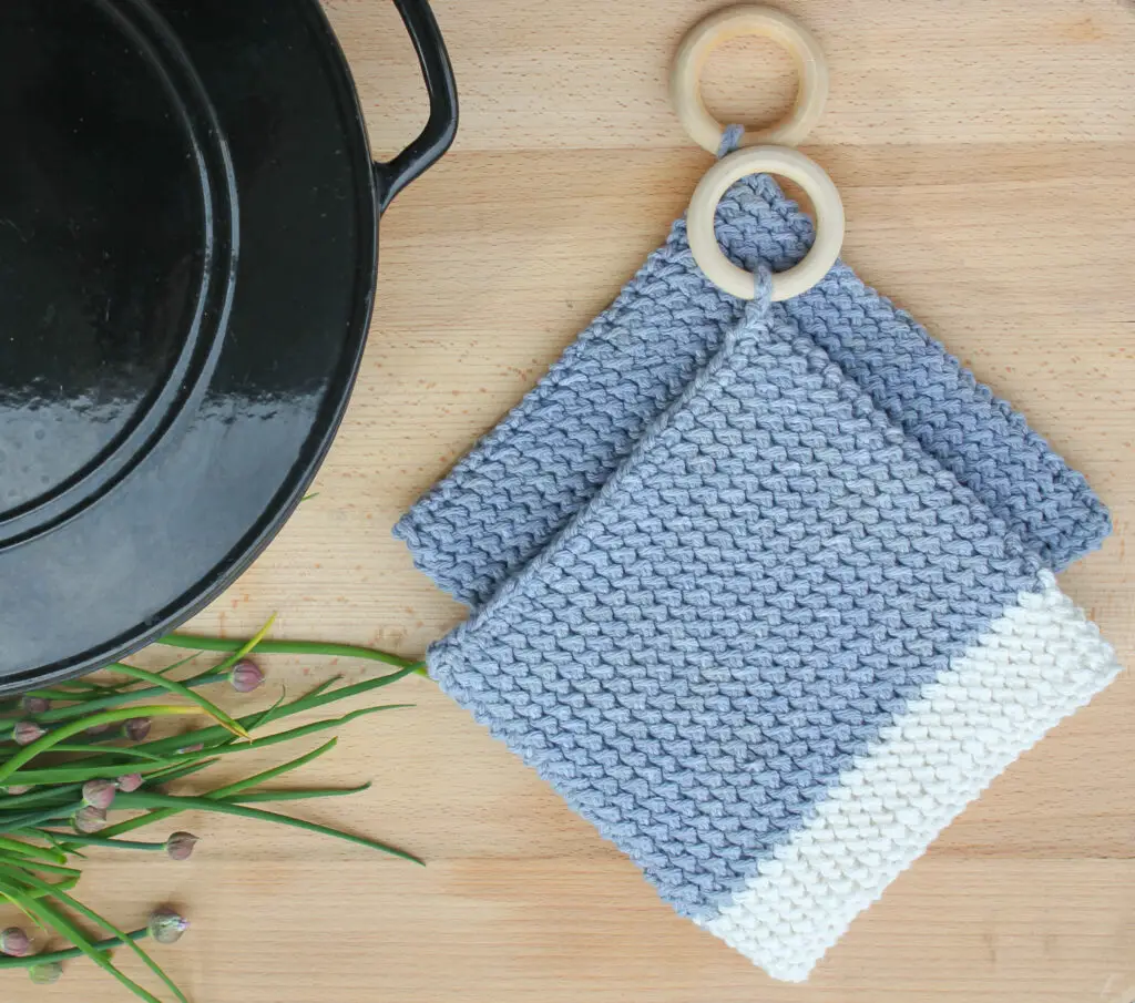 Blue crochet pot holders next to a dutch oven on a wooden cutting board.