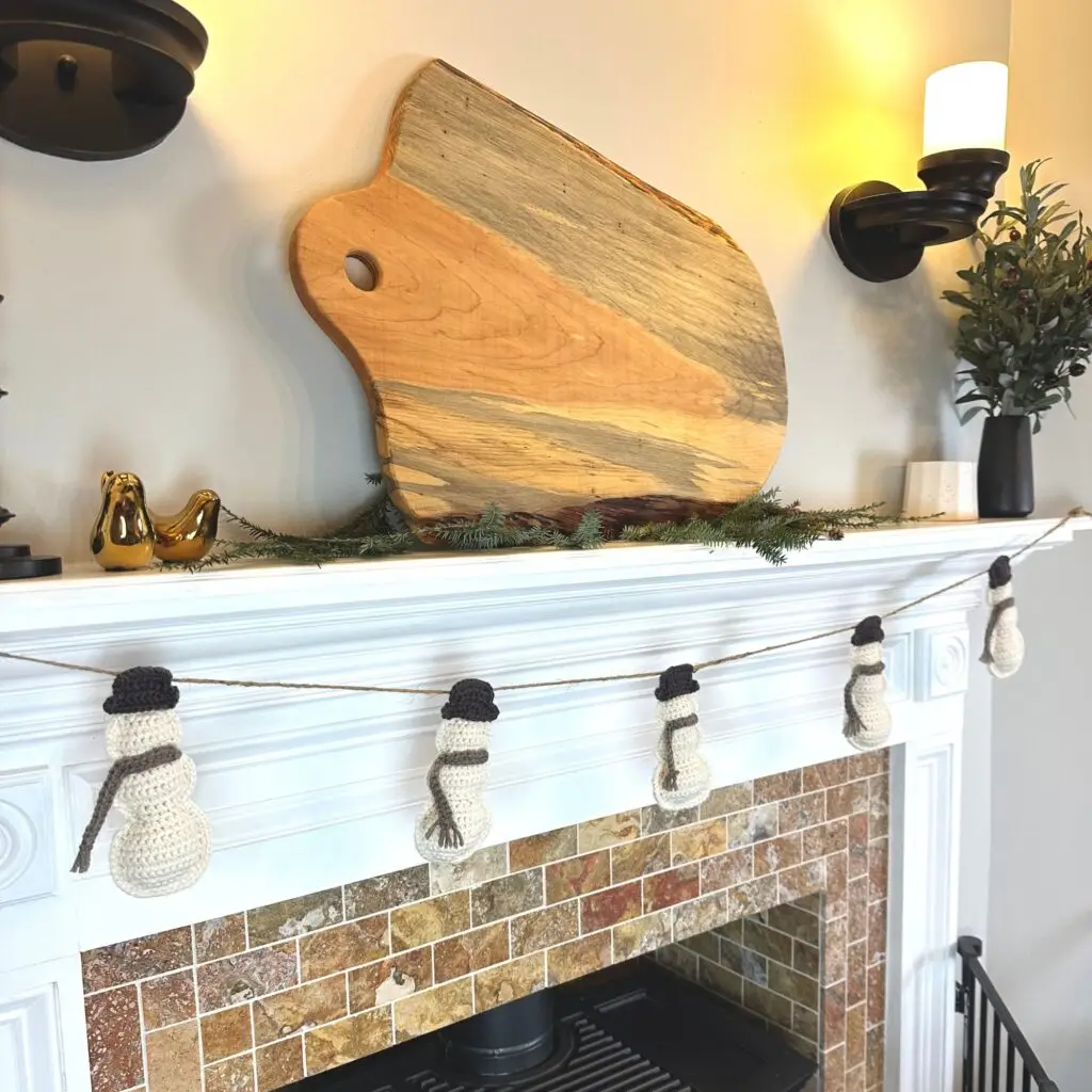 crochet snowman garland hung on a fireplace
