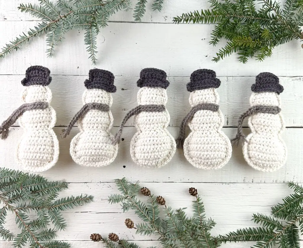 crochet snowman on a white background with pine boughs