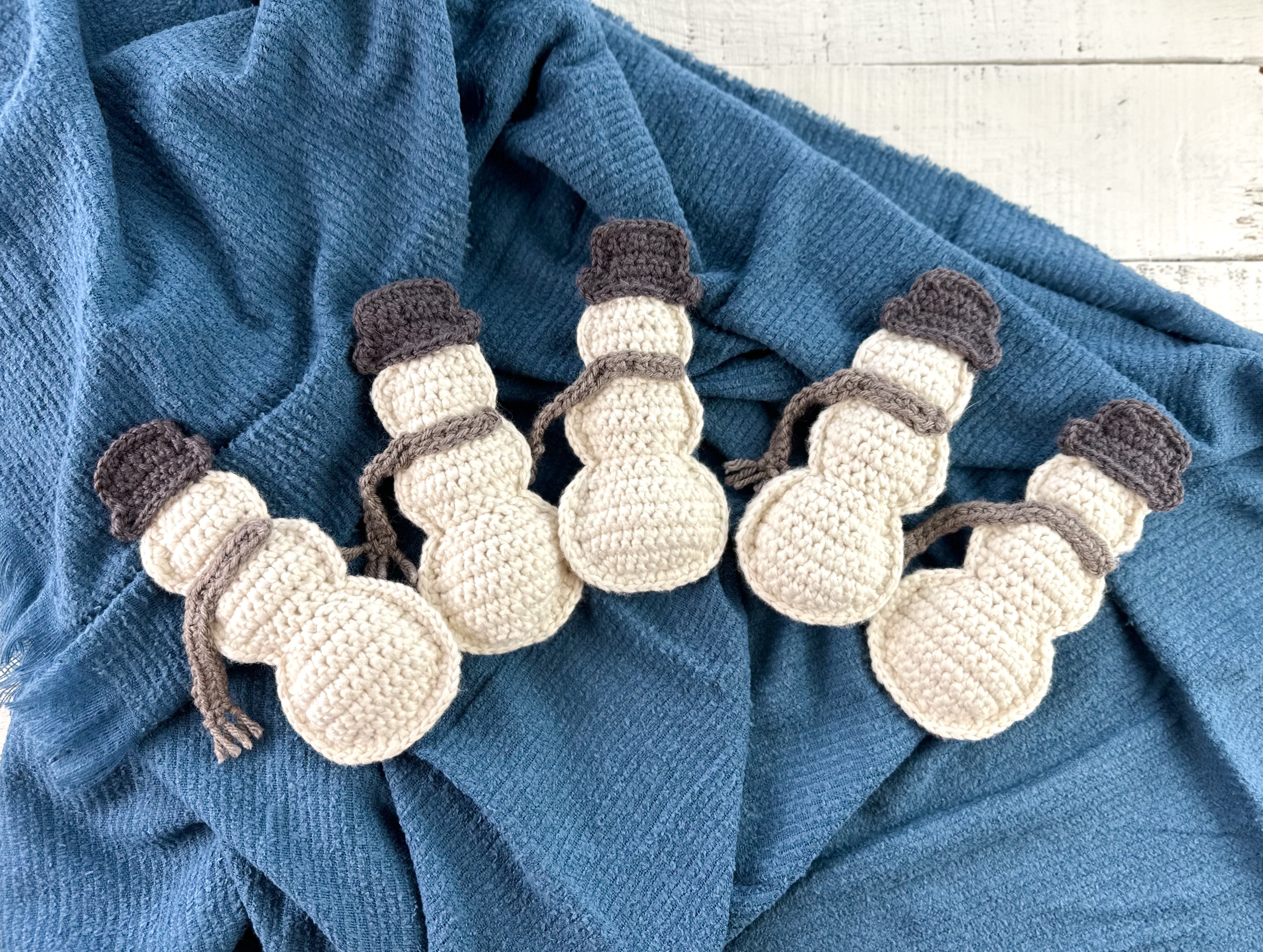 crocheted rustic snowmen with hats and scarves on a blue blanket background