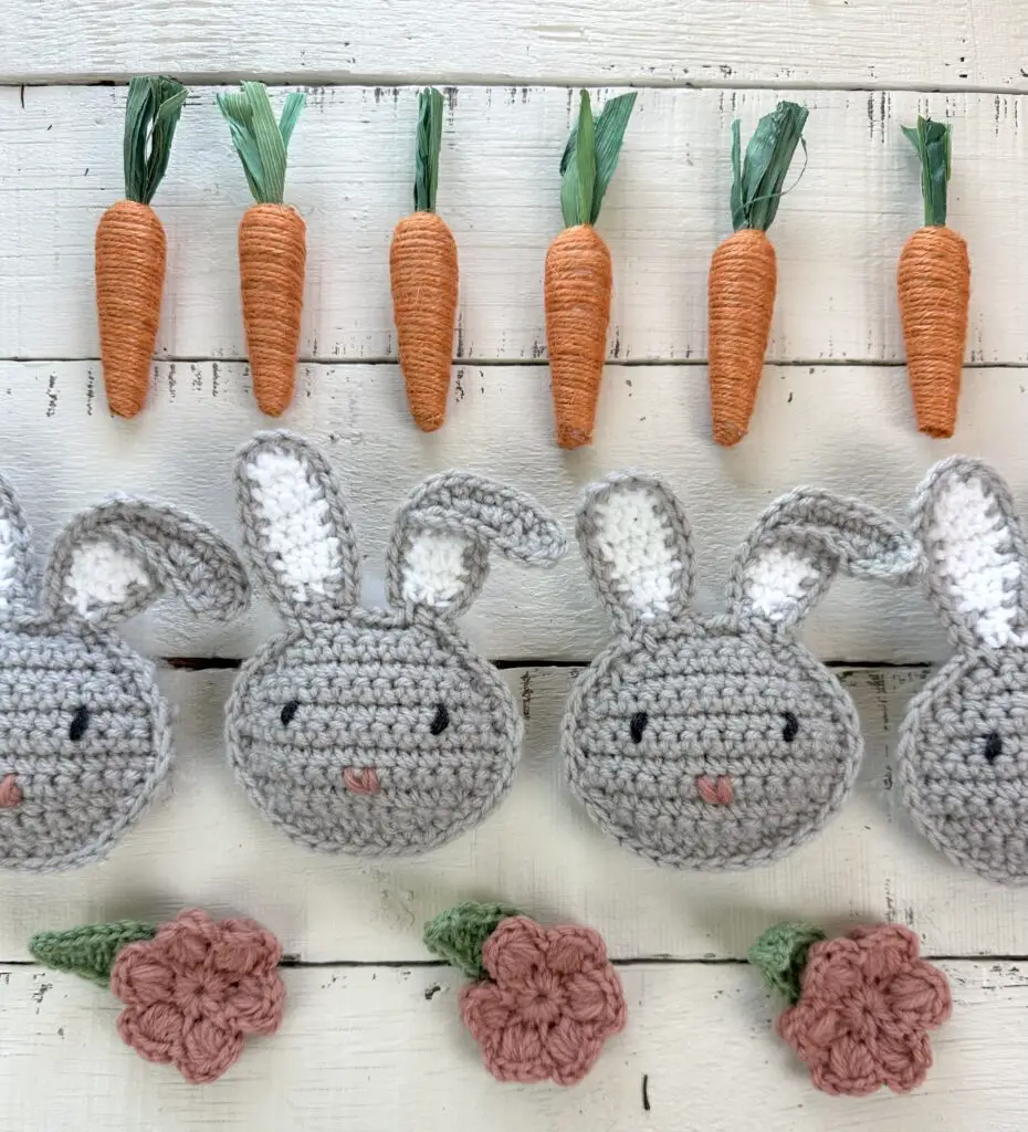 crocheted bunnies and pink mollie flowers on a table with orange decorative carrots