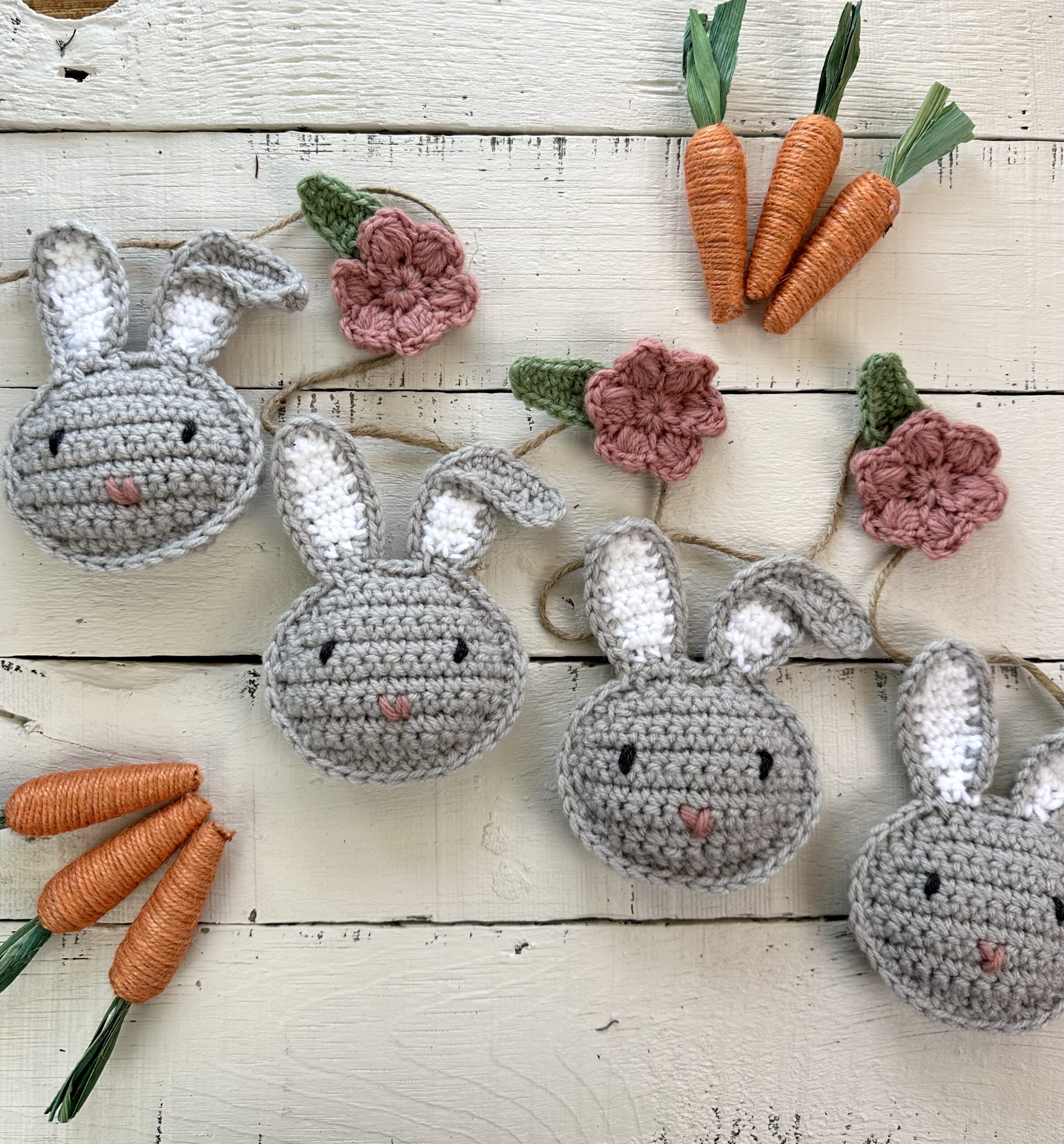 gray crocheted bunnies and pink crocheted mollie flowers on a table with orange decorative carrots